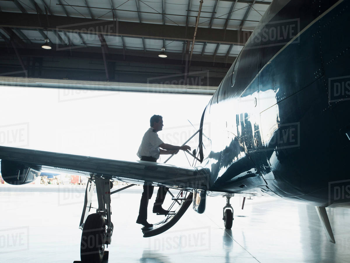 Caucasian pilot boarding airplane in hangar Stock Photo Dissolve