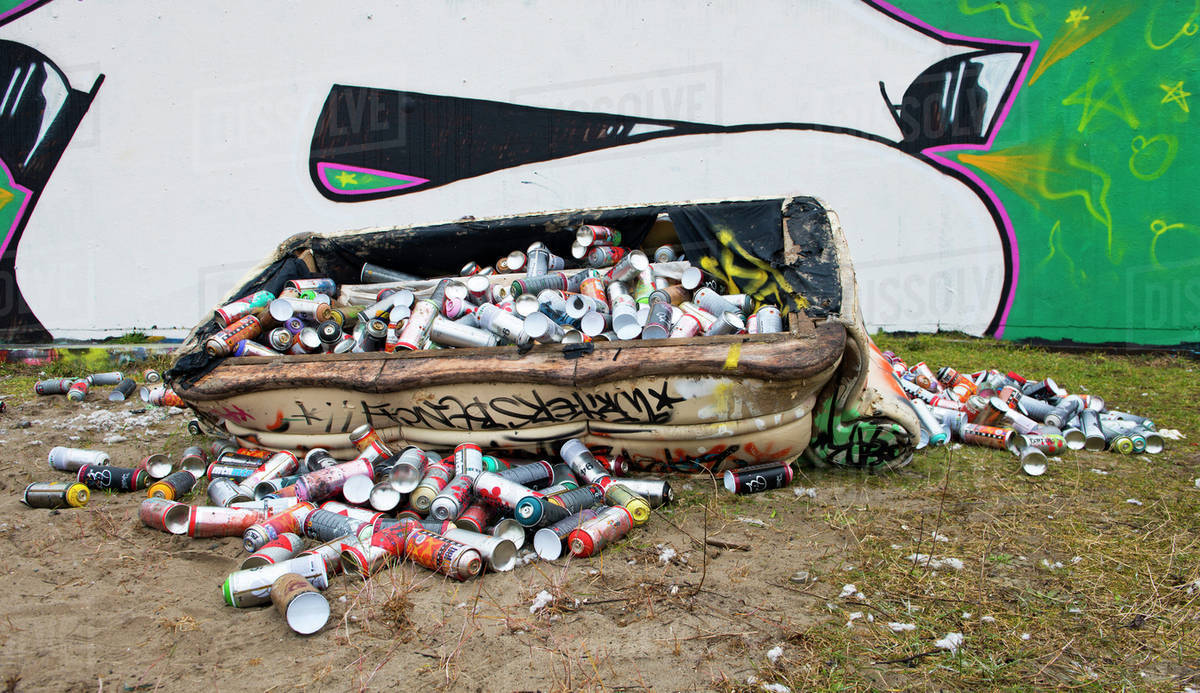 Dumpster filled with spray paint cans on city street with graffiti