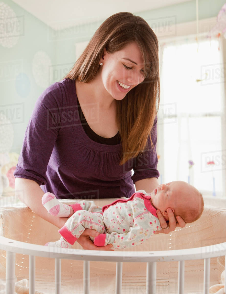 Caucasian mother lifting baby girl from crib Stock Photo Dissolve