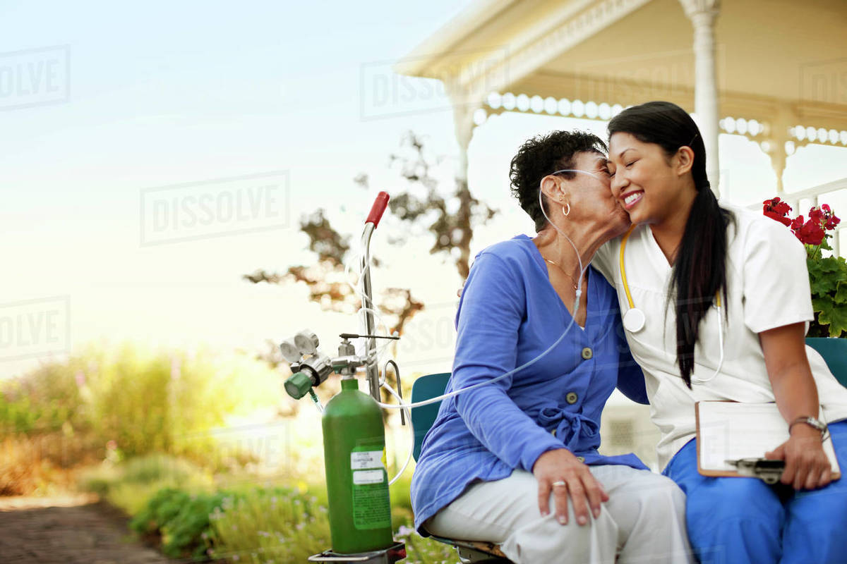 Young female nurse sitting in the garden of an elderly patient with an oxygen tank. Royalty-free stock photo