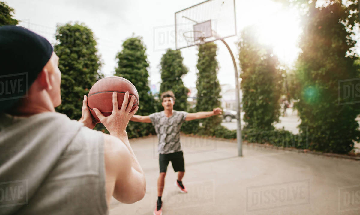 Young man taking shot with friend blocking on basketball court