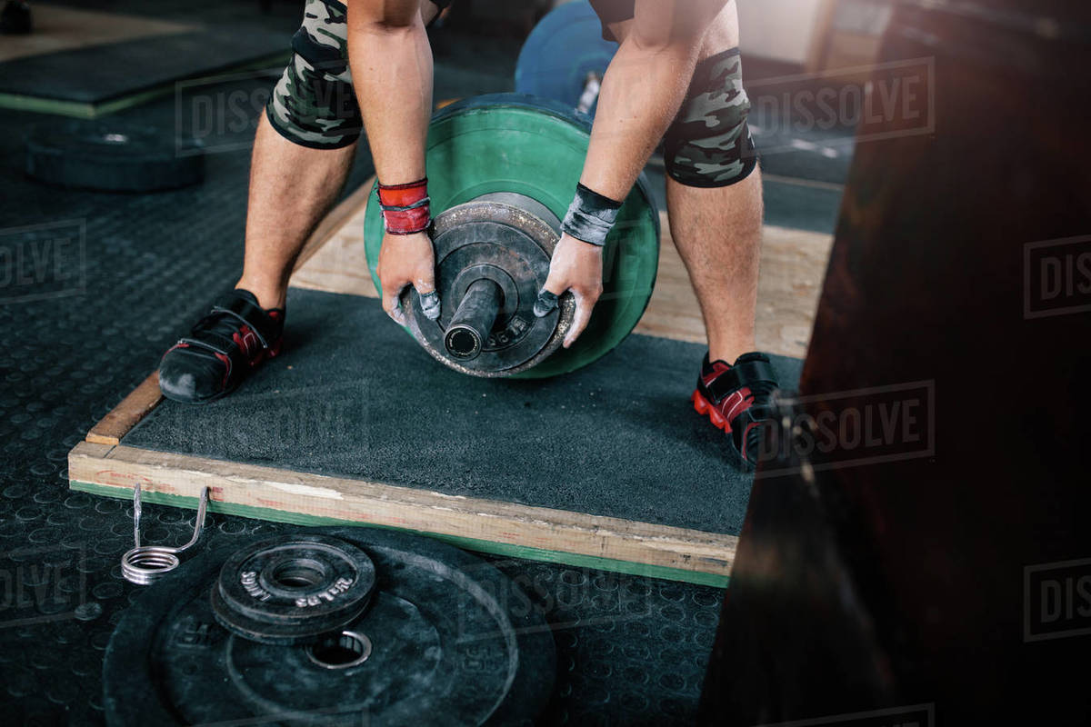 Cropped shot of male bodybuilder hands adding weights to barbell