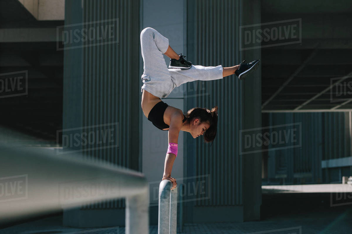 Woman doing a handstand on railing outdoors. Flexible female performing extreme sports in urban city space. Royalty-free stock photo