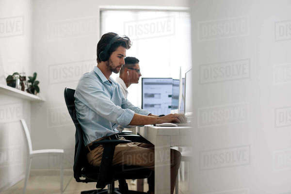 Software developers sitting at office working on computers wearing ...