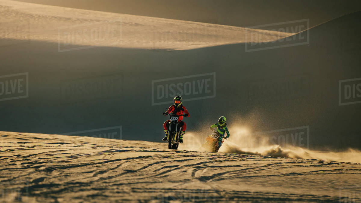 Motocross racers riding bikes in desert. Bikers racing on sand dunes