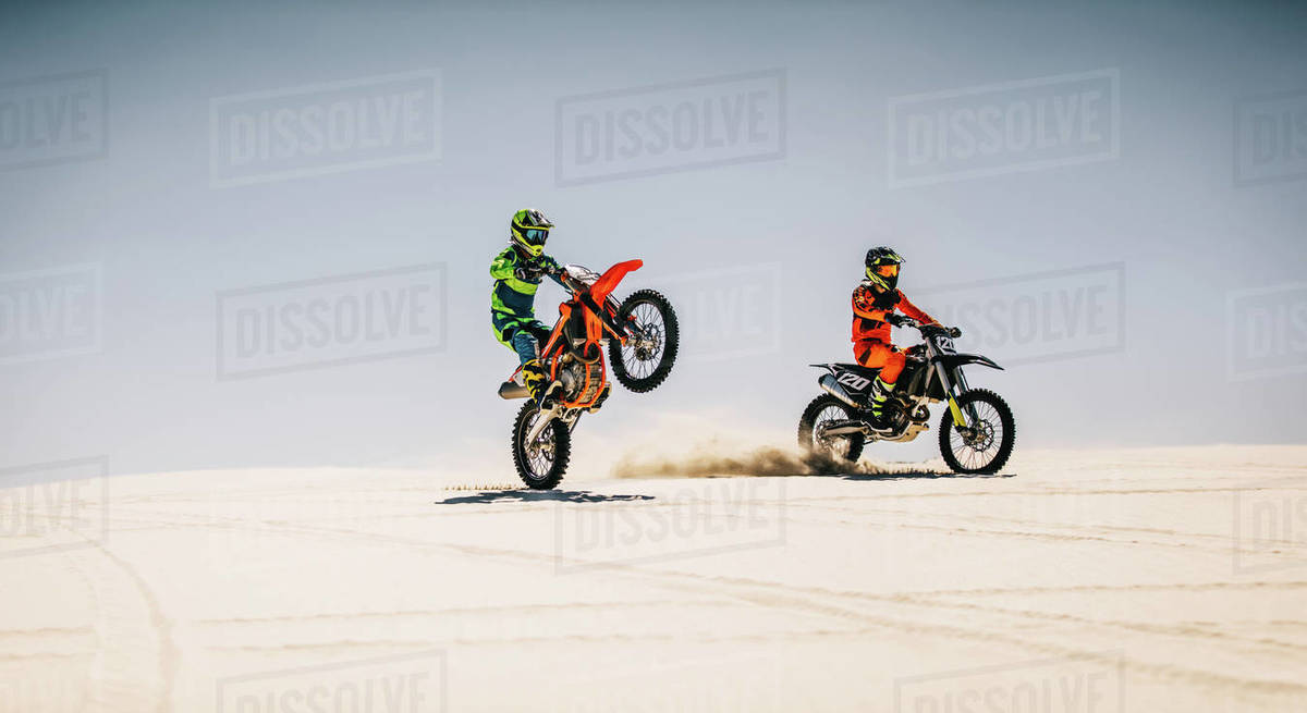 Two motocross riders riding bikes in desert. Professional dirt bikers