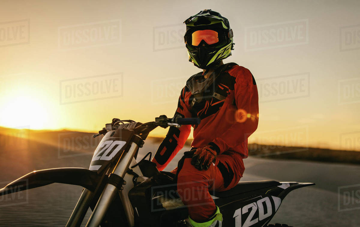 Professional motocross rider sitting on his bike in a desert. Motorcycle rider ready to race on the sand dunes during sunset. Royalty-free stock photo