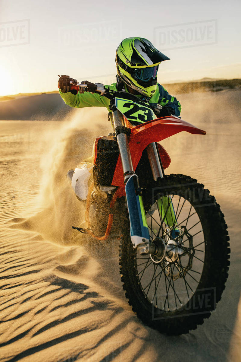 Motocross rider riding his bike on a sand dune. Motorcycle rider in racing gear riding his bike up the sand dune leaving behind sand dust. Royalty-free stock photo