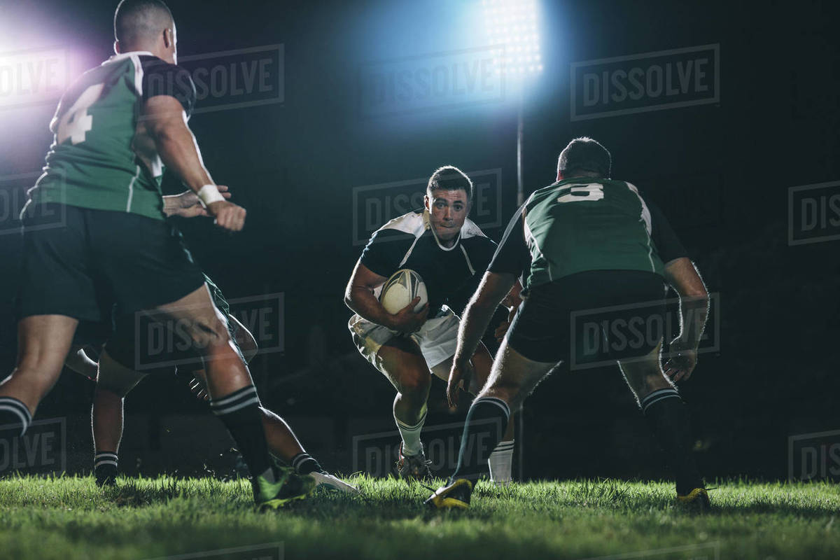 Rugby player running on field with ball and tackling with opposite team