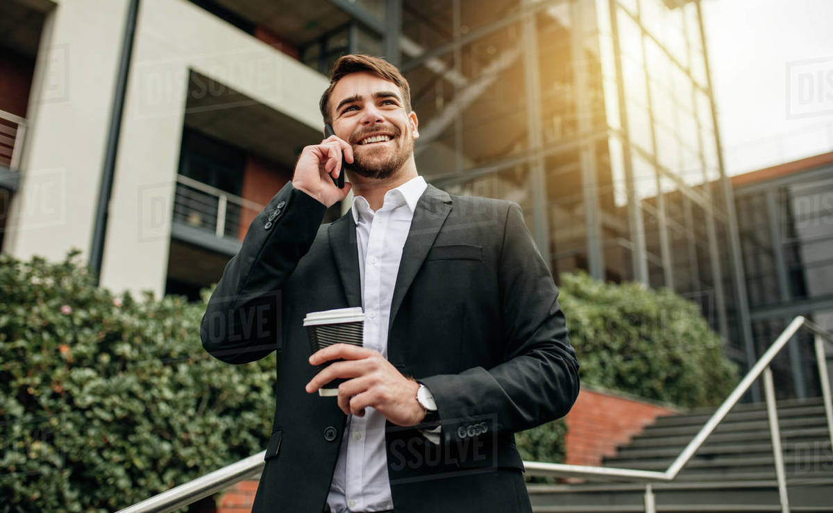 Businessman walking out of office with coffee and talking over cell phone. Businessman in formalwear walking down the steps making a phone call. Royalty-free stock photo