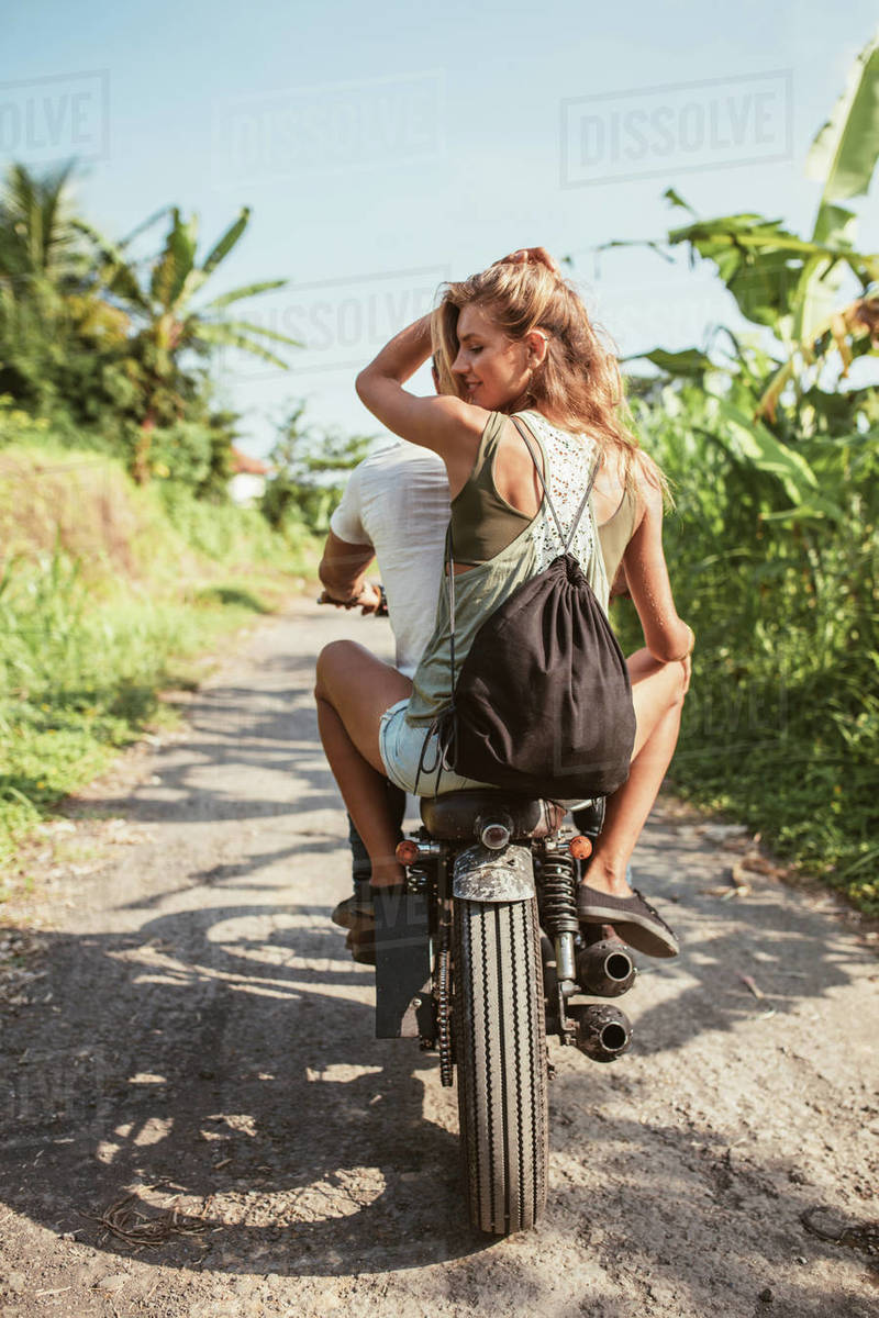 Rear view shot of young couple riding motorcycle on rural road