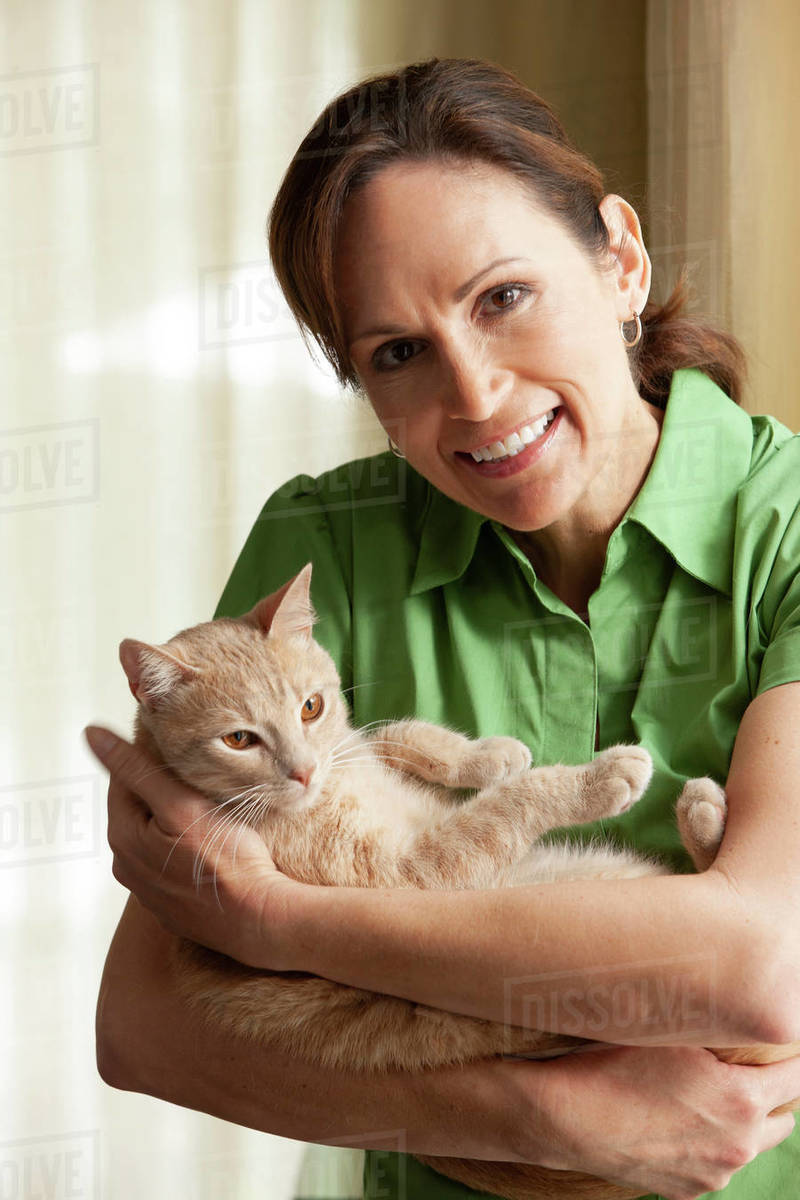 Middle aged Caucasian woman standing by window holding cat cradled in