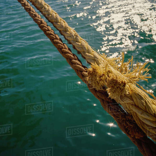 Thick ship's ropes securing ship to wharf against sparkling water ...