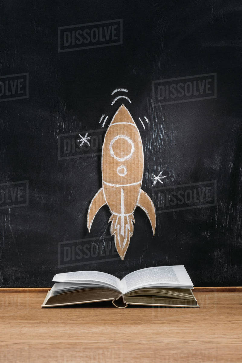 Close up view of cardboard rocket on blackboard and opened book on