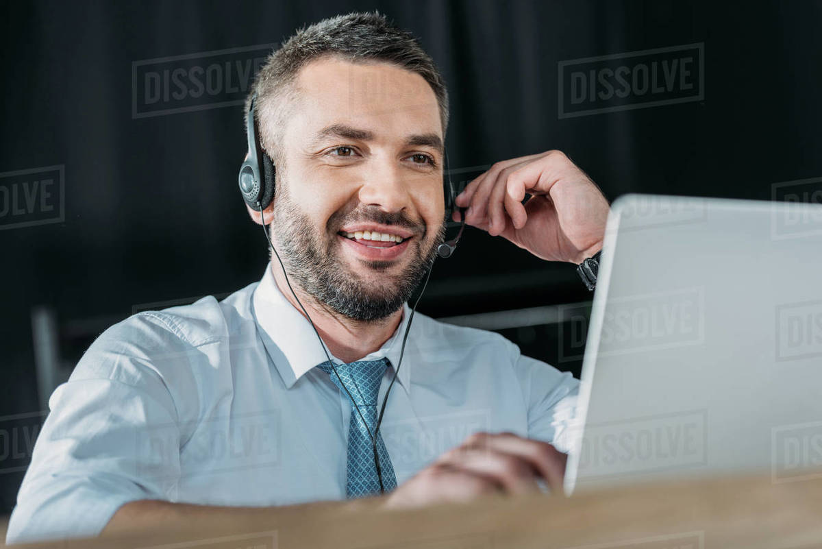 Smiling support hotline worker with laptop and microphone at work