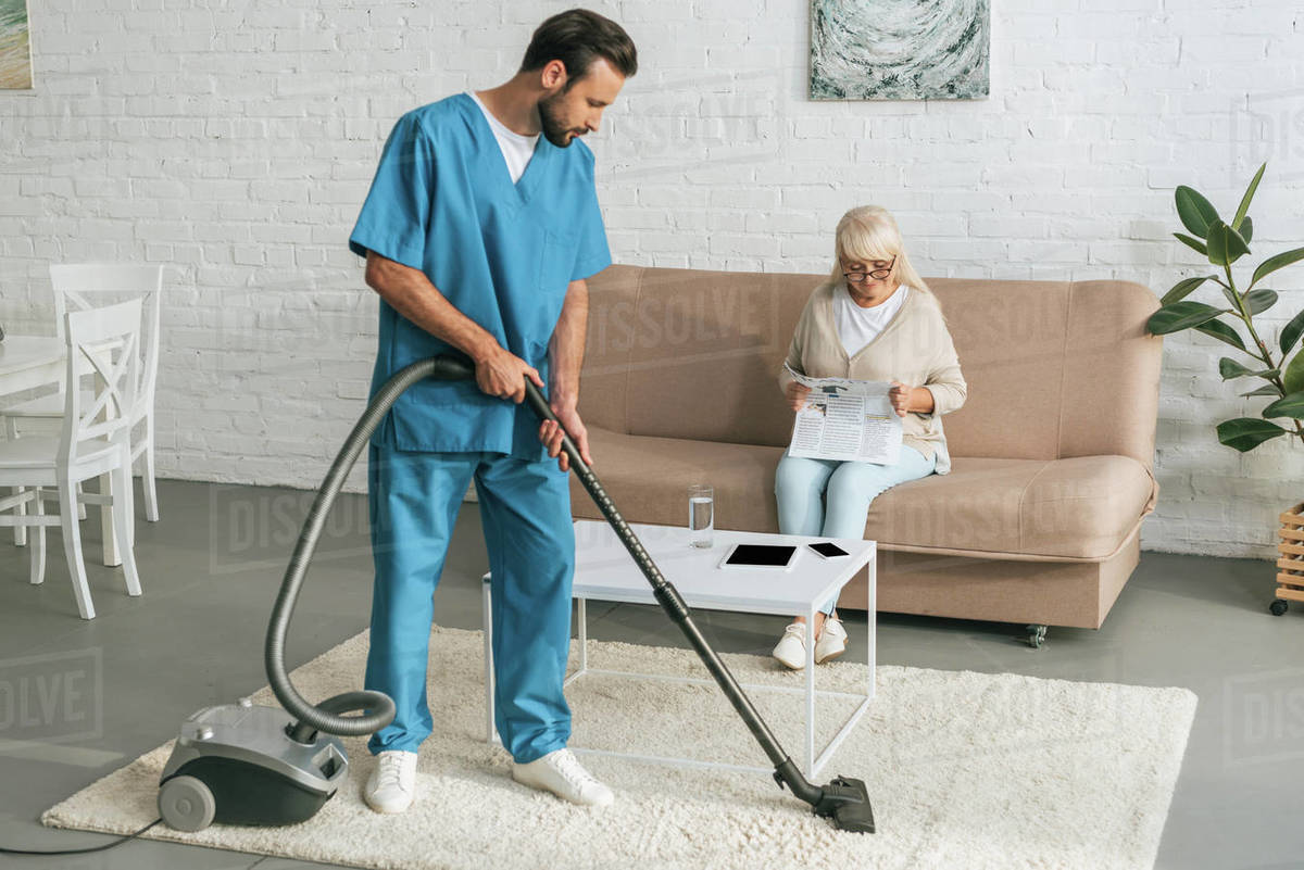 Young Social Worker Cleaning Carpet With Vacuum Cleaner While