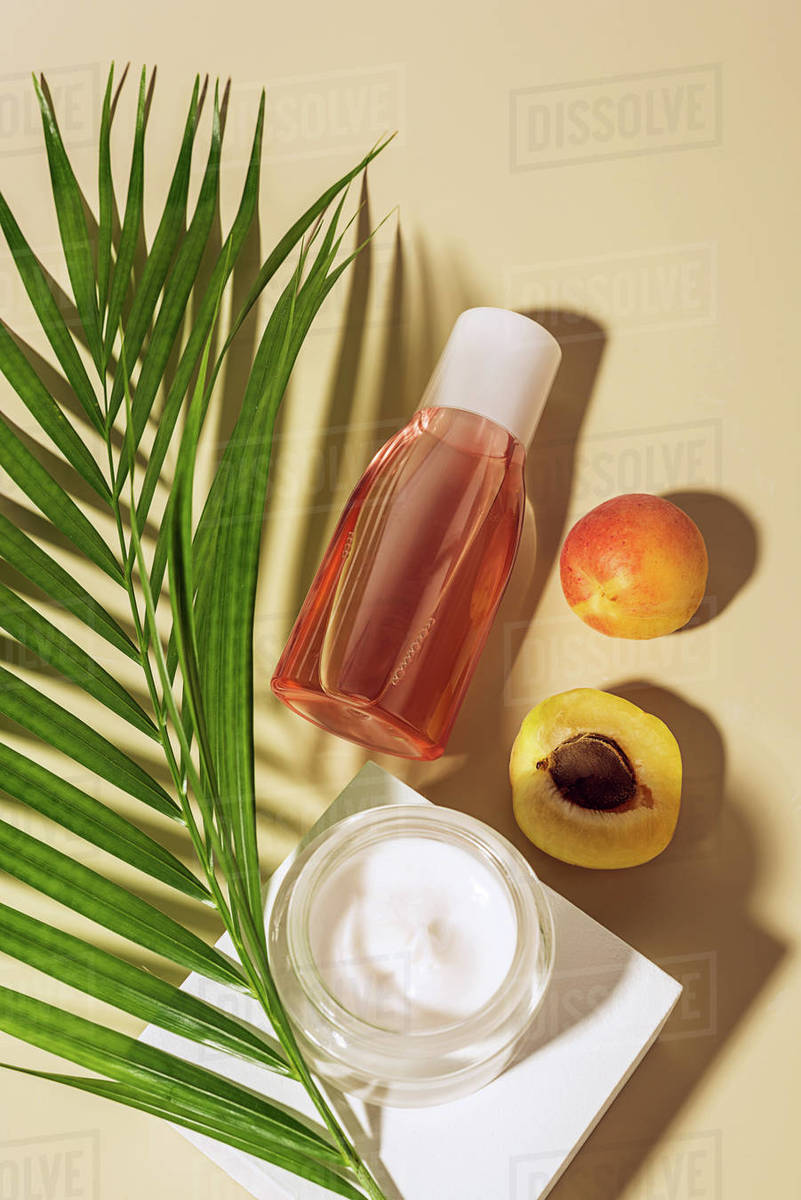 flat lay with body cream and lotion, apricots and green palm leaf on