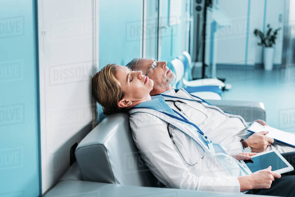 Side view of tired male and female doctors sleeping with clipboard and
