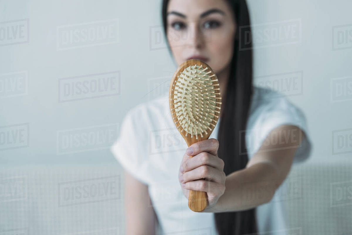 Closeup view of young woman holding hairbrush with fallen hair on grey