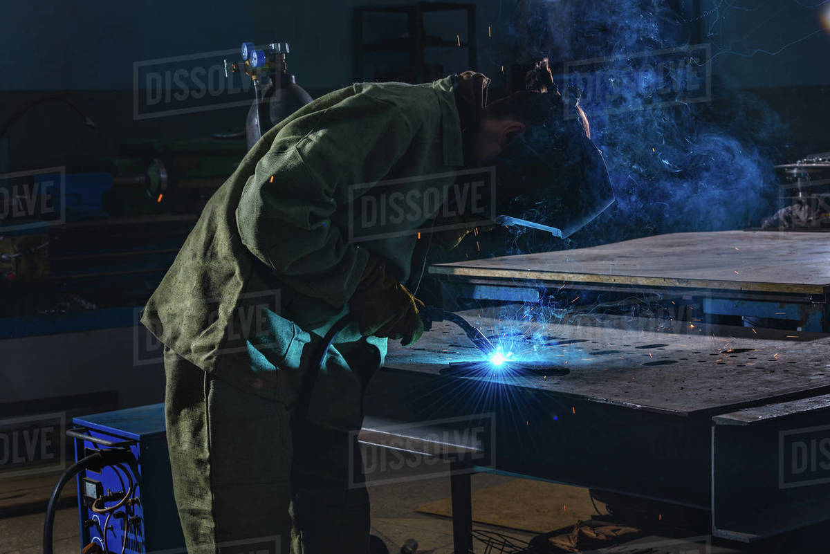 Side view of welder in protection mask brazing metal at factory Stock