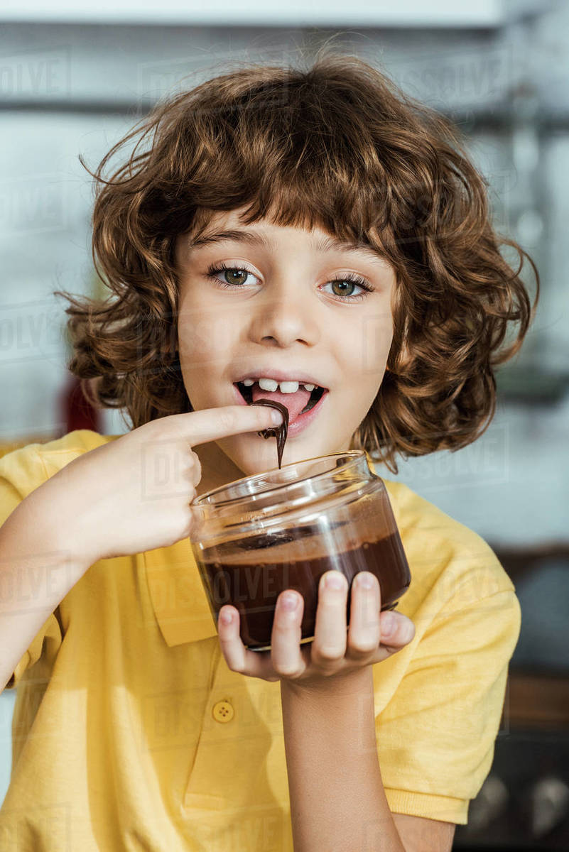 Adorable happy child eating chocolate spread from container and smiling