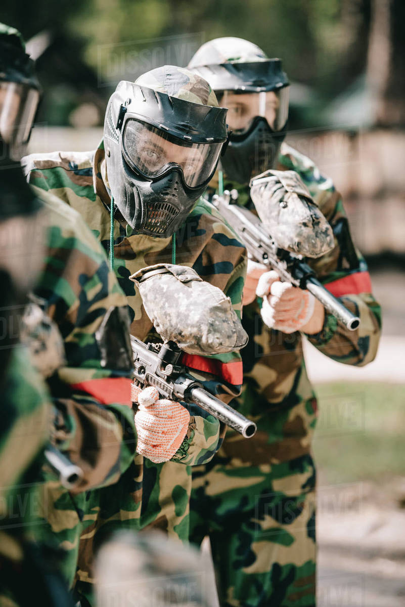 Paintball players in goggle masks and camouflage uniform holding