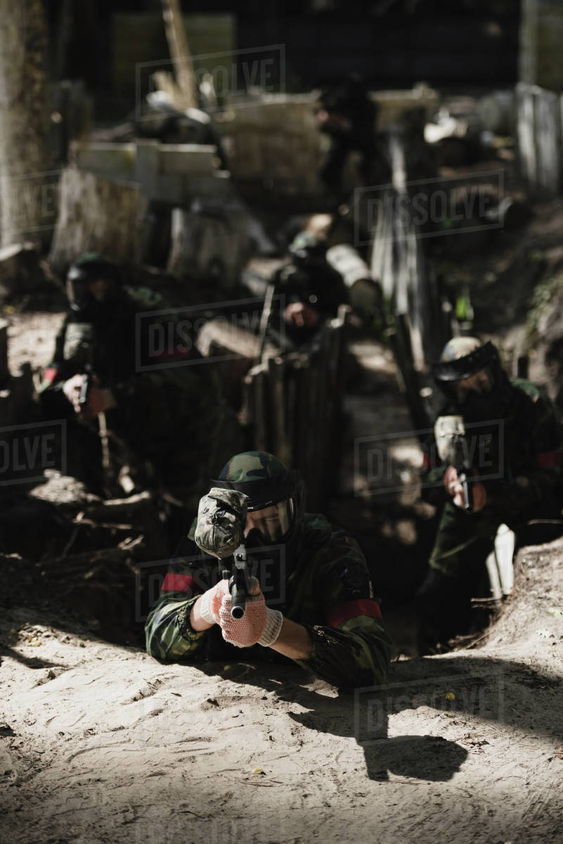 Paintball team in camouflage and protective masks aiming by marker guns