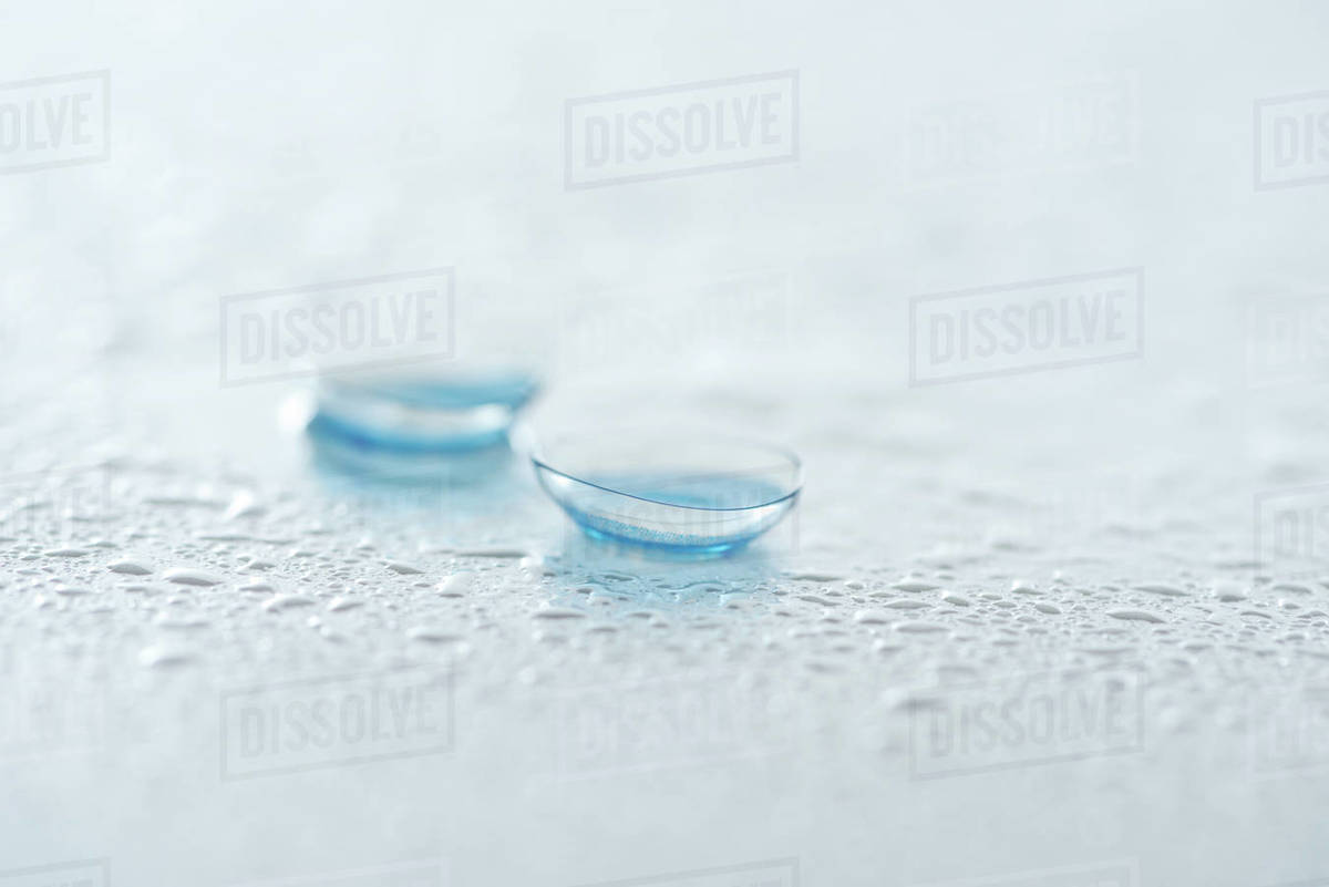 Close up view of contact lenses on white background with water drops
