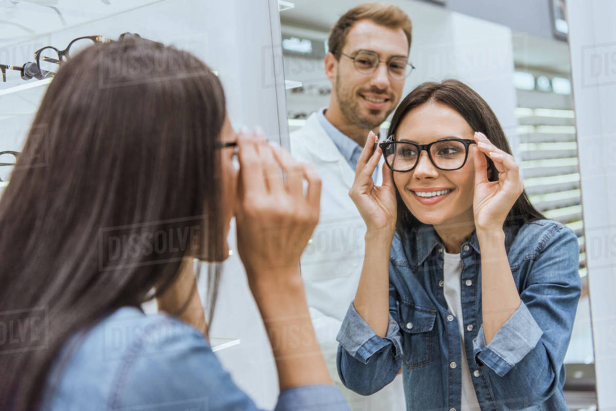 Rear view of cheerful woman choosing eyeglasses and looking at mirror