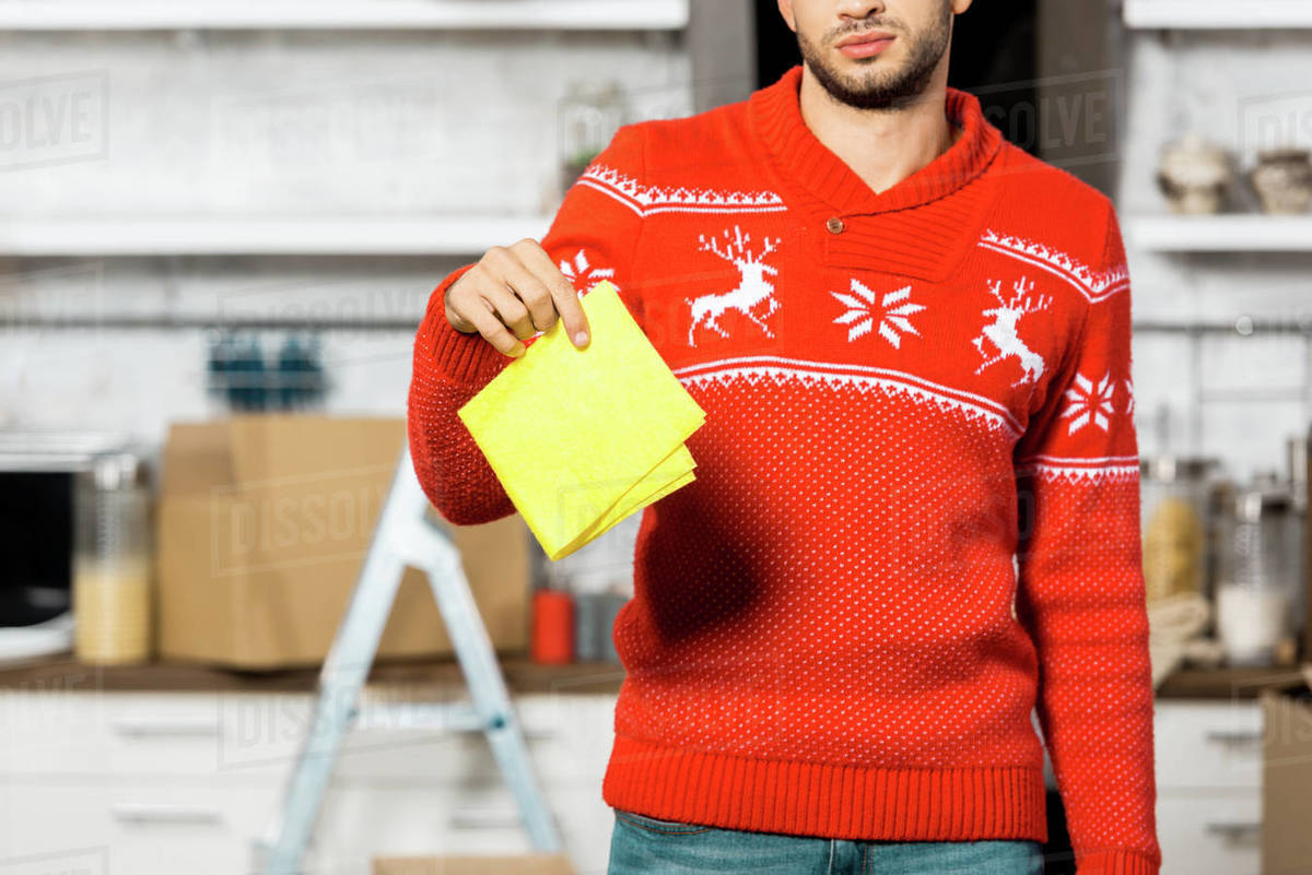 partial view of young man holding yellow dirty rag in kitchen during ...