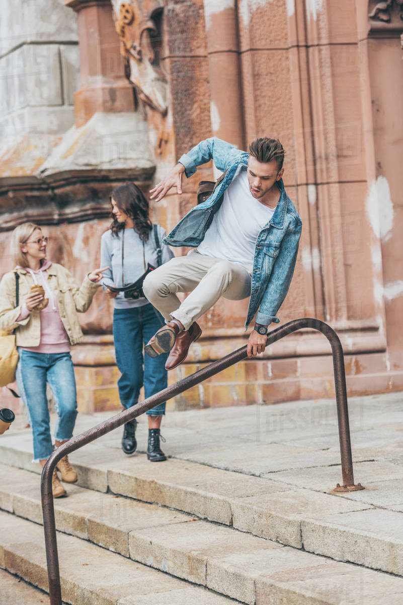 Beautiful girls spending time together in city while man jumping over
