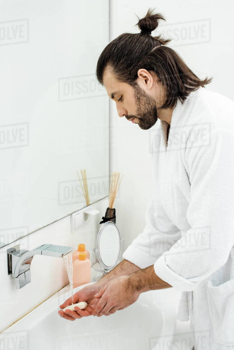Adult handsome man in bathrobe washing hands in bathroom Stock Photo