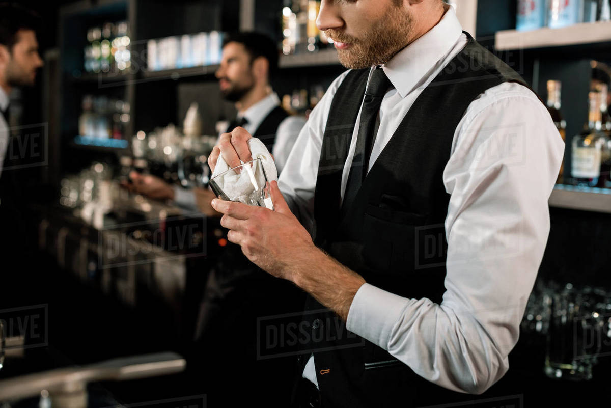 Bartender cleaning glass with white cloth in bar Stock Photo Dissolve