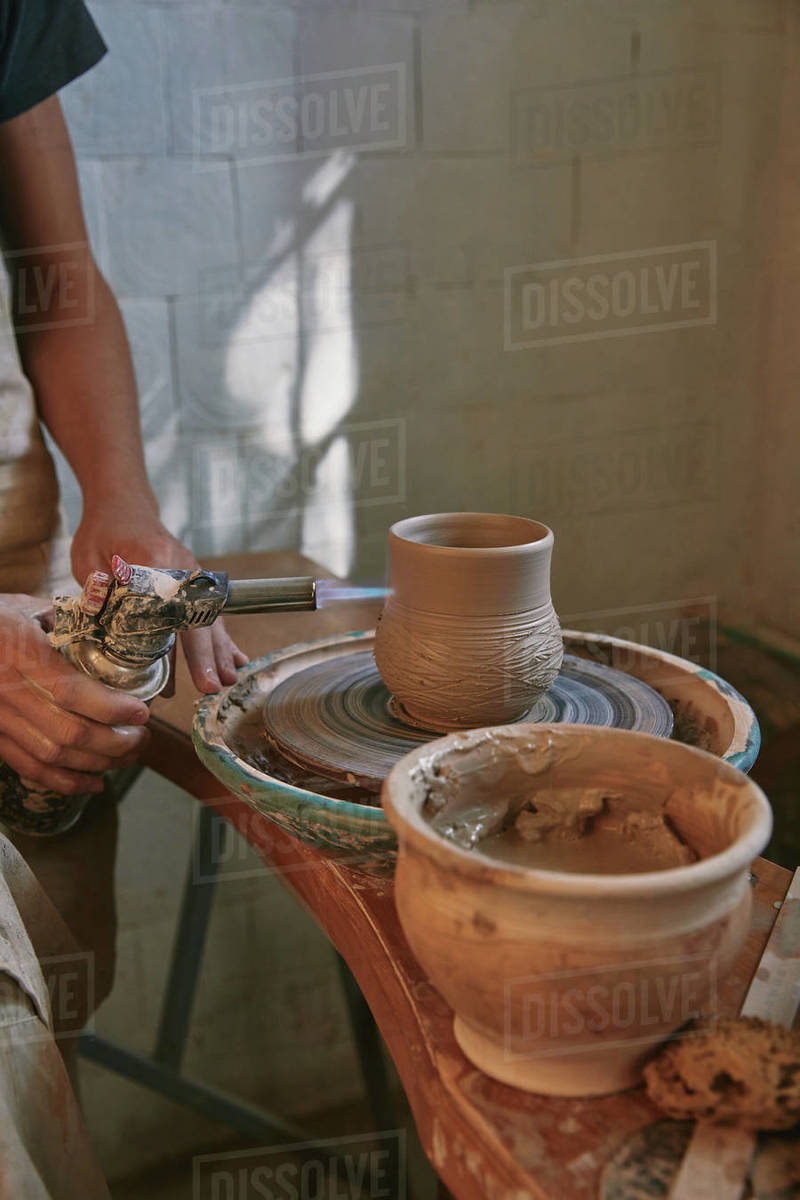 partial view of male potter in apron firing clay pot at pottery studio Stock Photo Dissolve