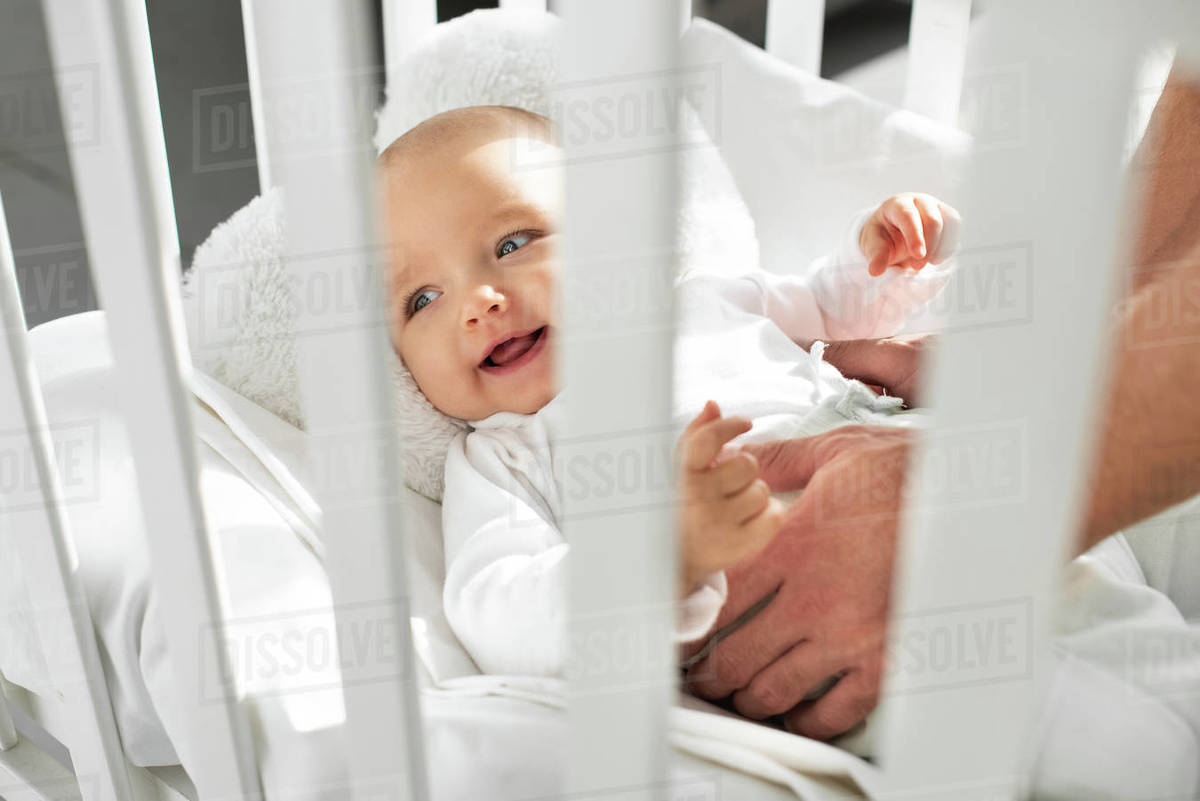 Cropped view of dad putting cheerful baby into baby crib Stock Photo