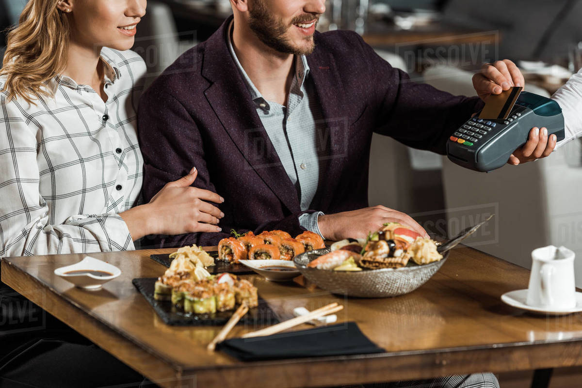 Partial view of couple sitting at table while man paying for dinner in restaurant Stock Photo