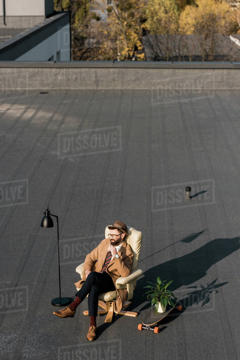 Adult businessman relaxing in armchair and smoking on roof - Royalty-free  Stock Photo