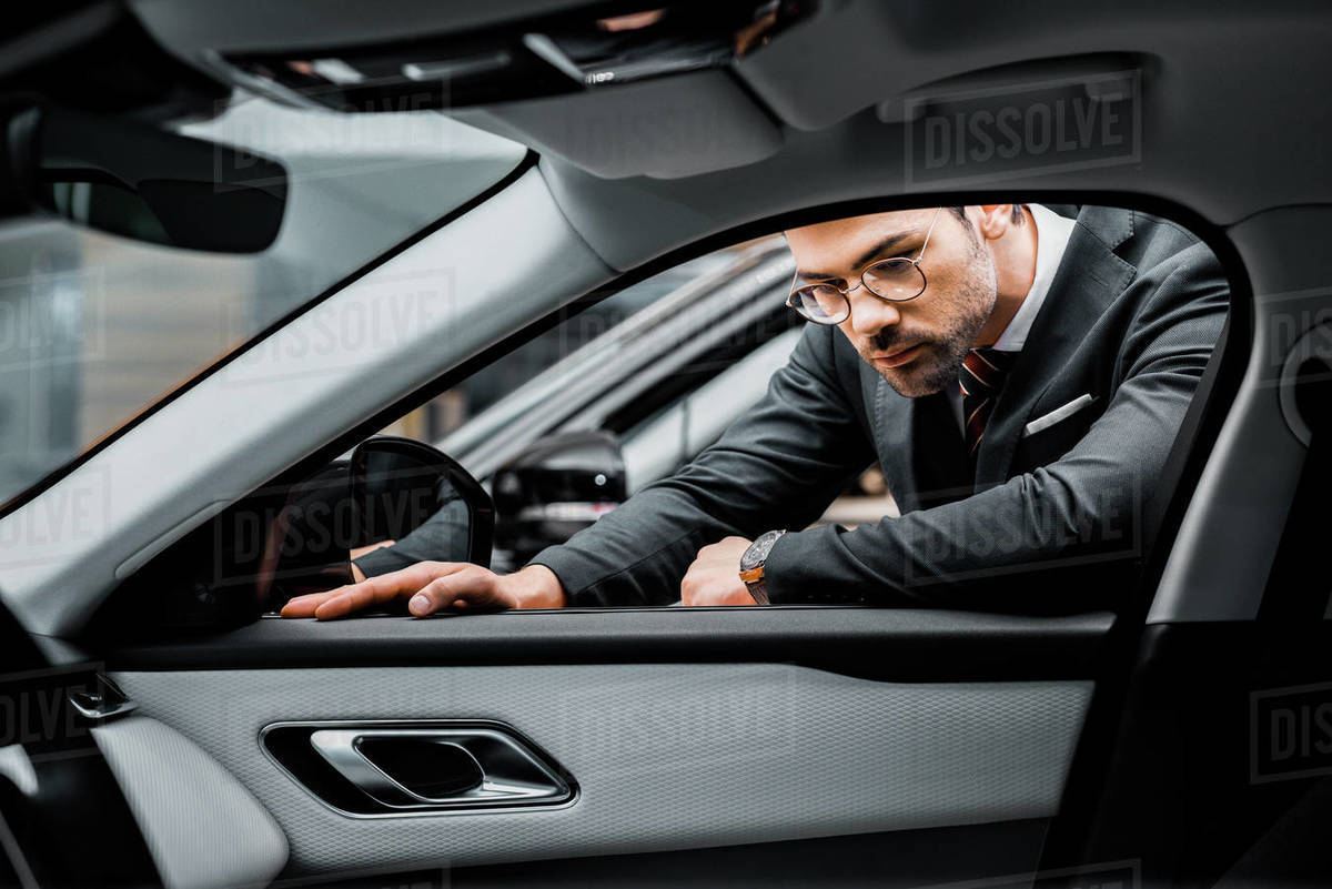 Serious businessman in eyeglasses choosing car in dealership salon Stock Photo Dissolve