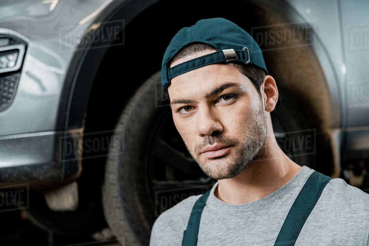 Portrait of young auto mechanic looking at camera with automobile
