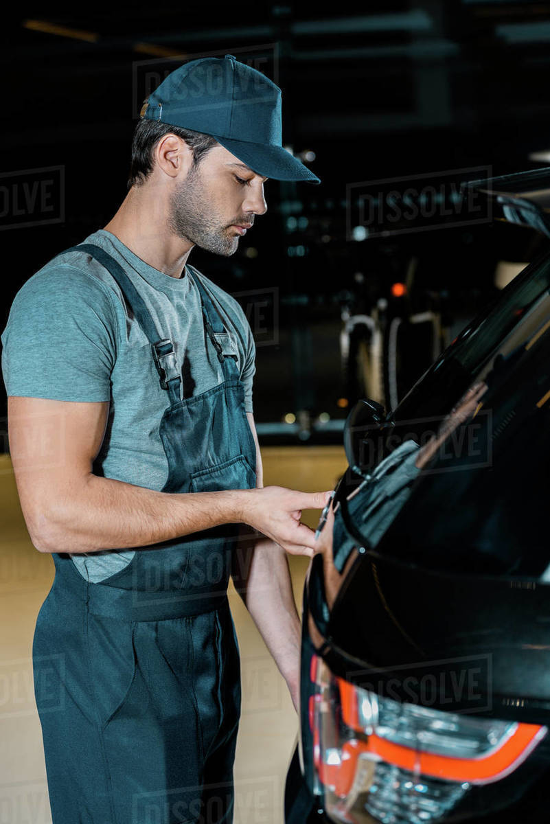 Side view of young auto mechanic checking car trunk at auto repair shop