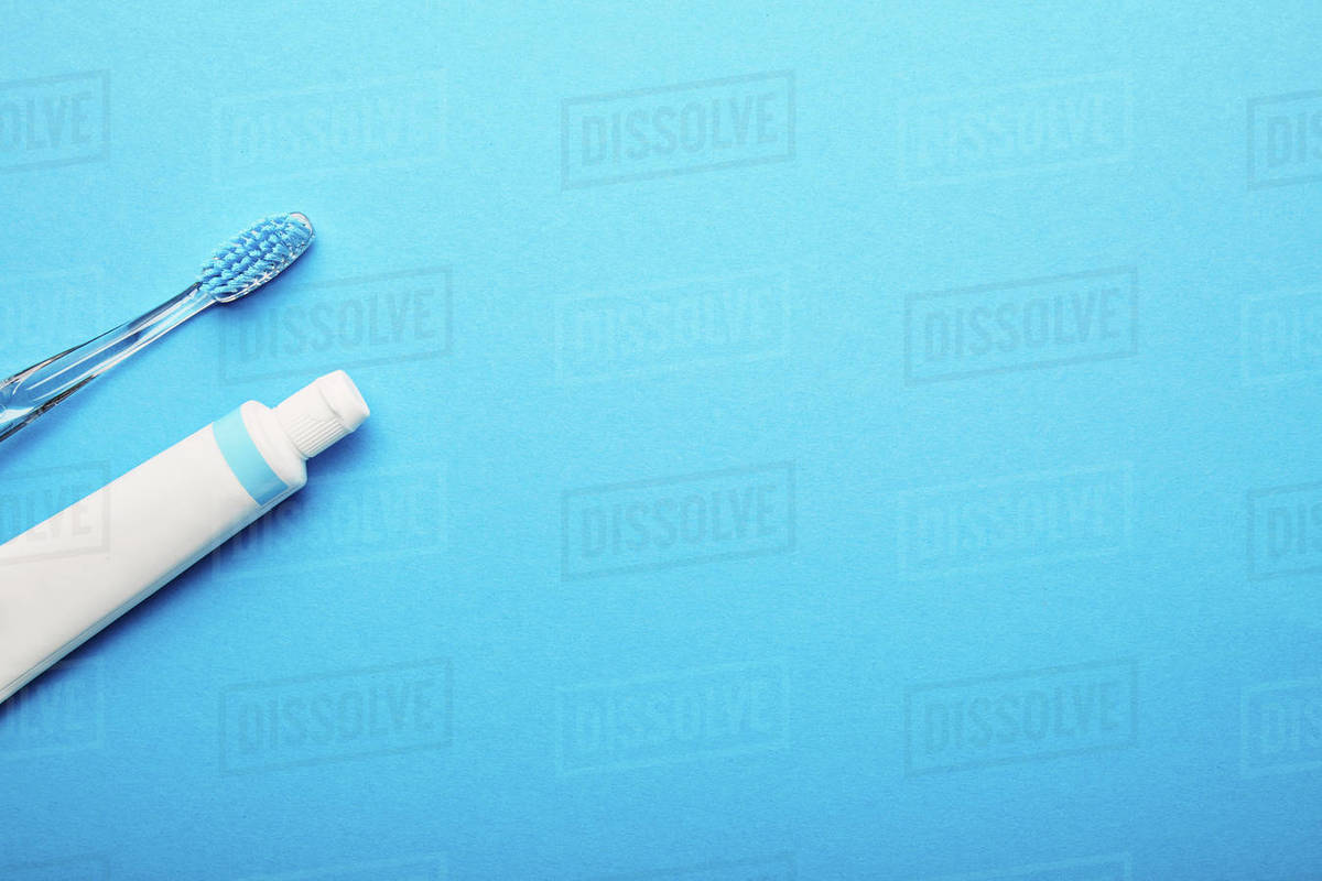 Top view of toothbrush and toothpaste arranged on blue backdrop