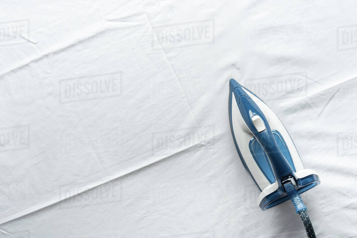 Top view of electrical iron standing on white bed sheets Stock Photo