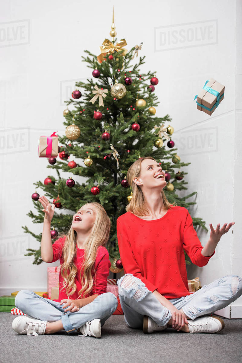Happy mother and daughter sitting at Christmas tree and throwing up