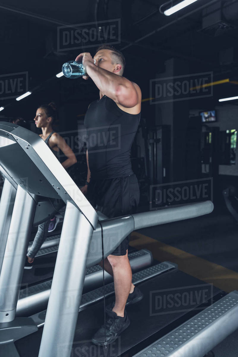 Man drinking water from sportive bottle while exercising on treadmill