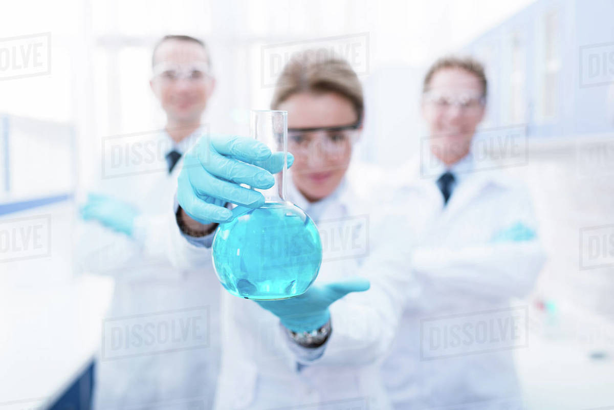 A doctor in latex gloves and lab coat showing flask with blue liquid