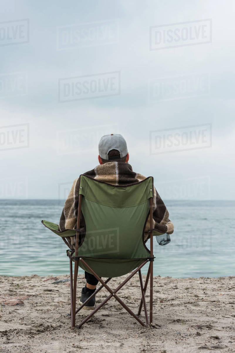 lonely man sitting on chair at seashore on cloudy autumn day