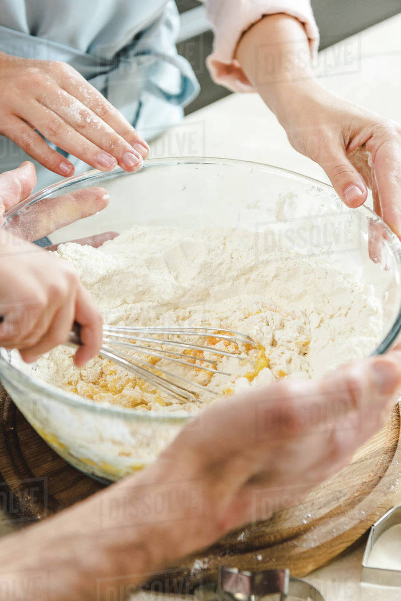 Cropped image of family hands mixing dough together in bowl - Stock