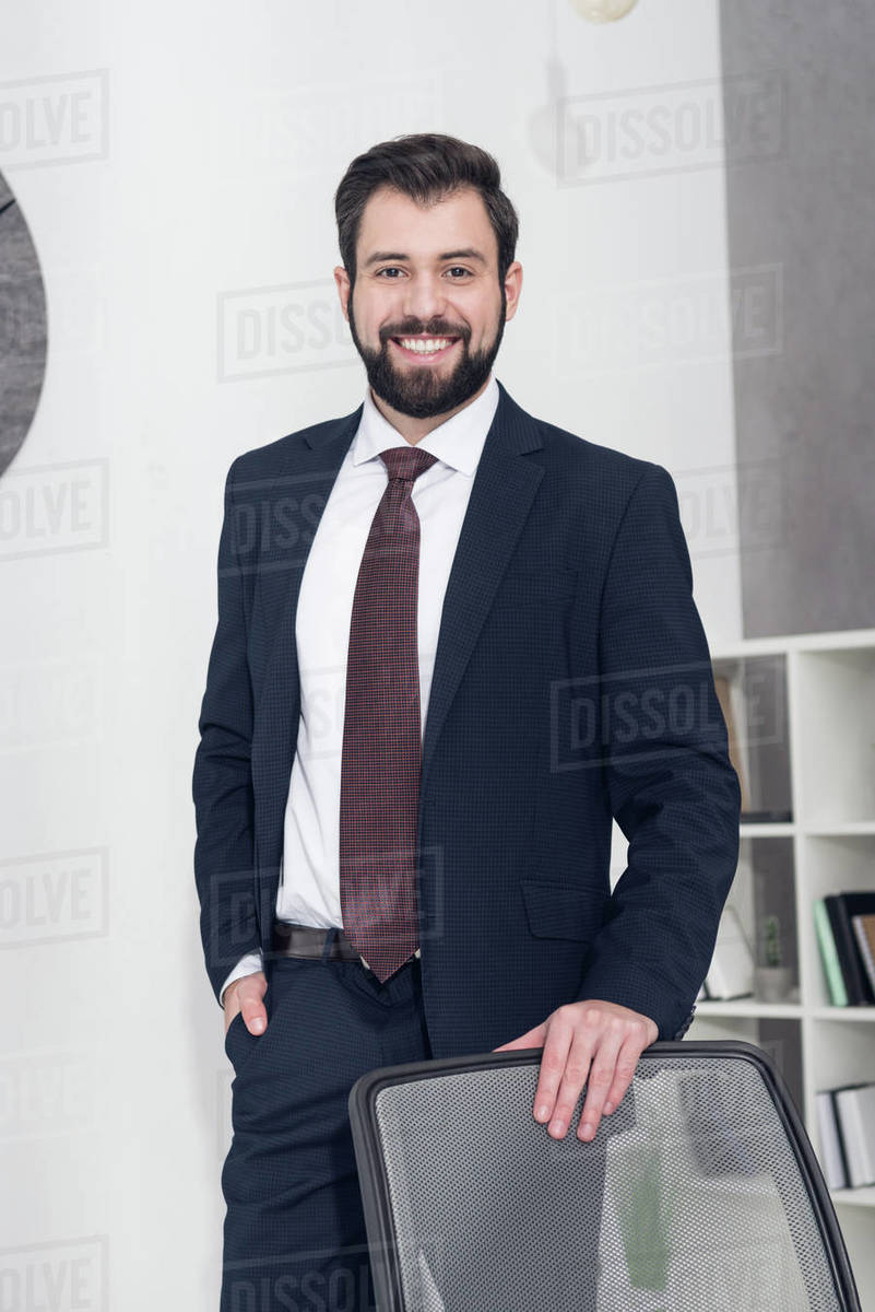 Portrait of cheerful businessman in suit standing at workplace in