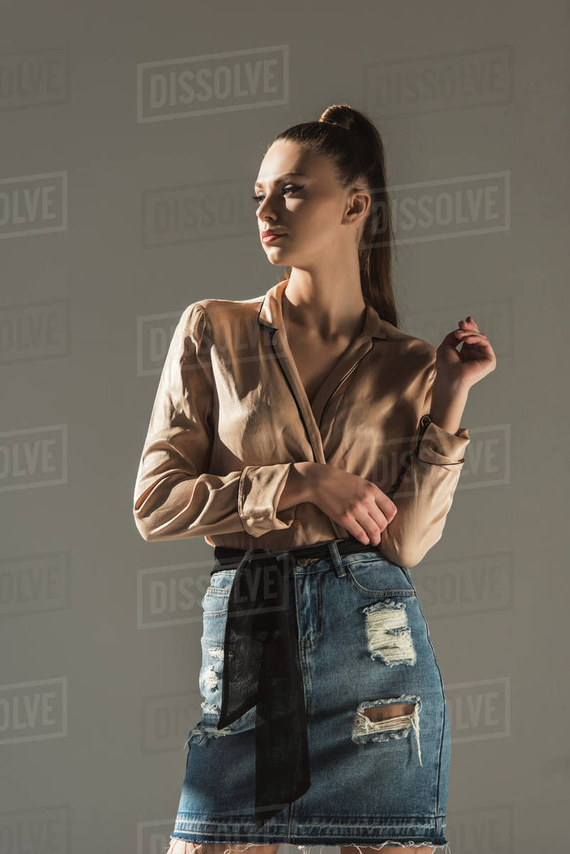 attractive girl posing in blouse and denim skirt, isolated on grey