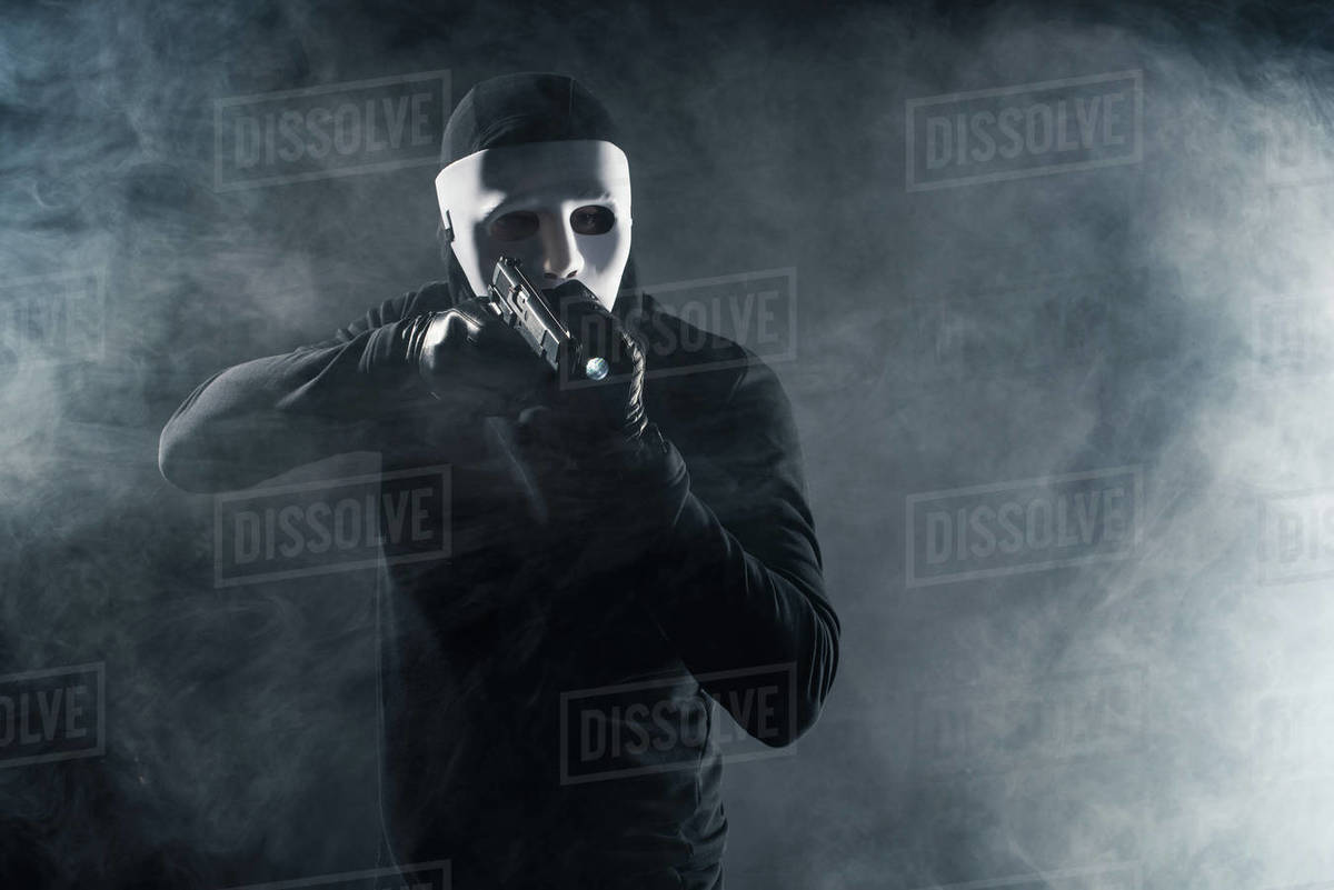 Man in mask and balaclava aiming with gun and flashlight Stock Photo